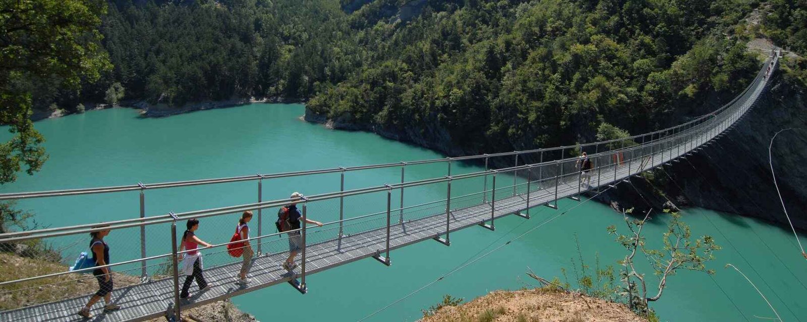 Randonneurs sur une passerelle himalayenne au-dessus du lac du Monteynard