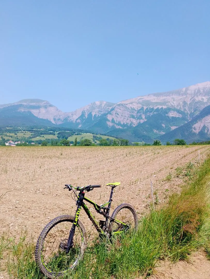 Un VTT posé au bord d'un champ, face aux falaises du Vercors